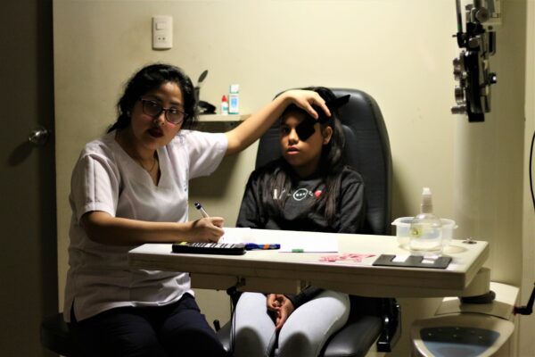 Woman providing eye exam to seated girl