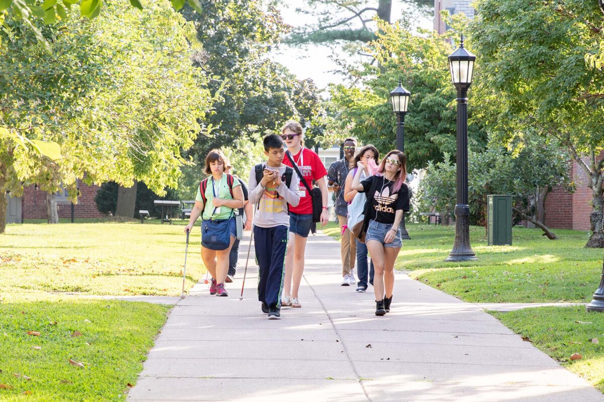 A group of diverse students walk on the Perkins campus, two of whom are holding canes.